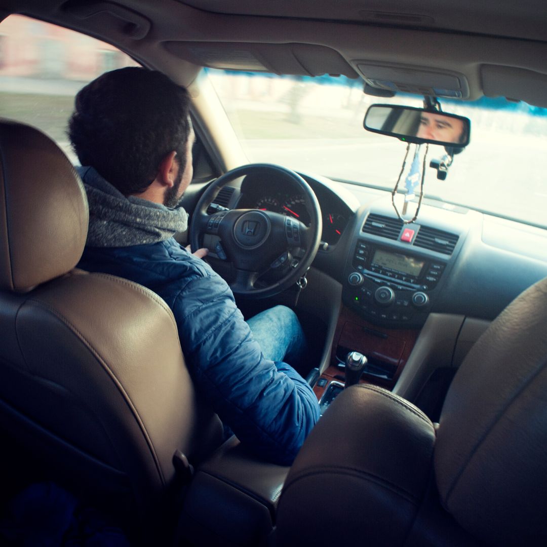 A man is driving a car, viewed from behind the passenger seat, setting the scene for a discussion about car problems.