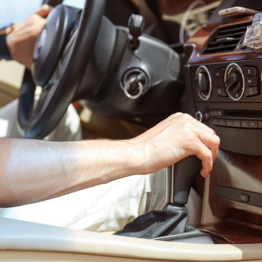 A person's hand is on the gear shift of a car, suggesting a problem with shifting gears.