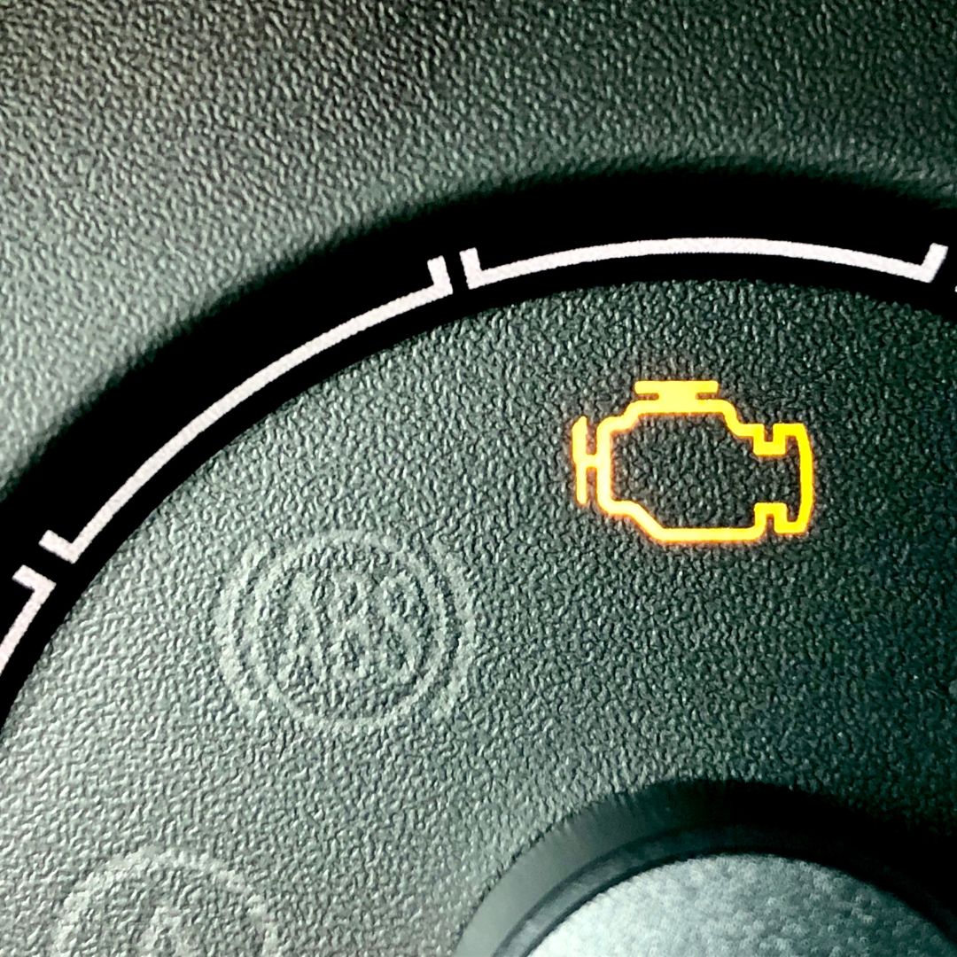 A close-up of a car's dashboard shows the glowing check engine light, a common indicator of various car problems including transmission issues.